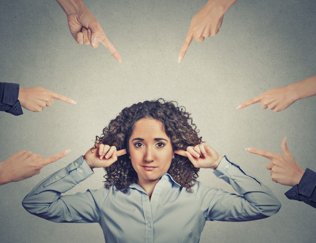 Many fingers pointing at a woman who is plugging her ears to avoid it all